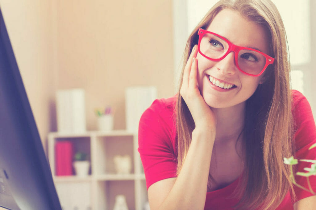 Happy young woman in glasses connecting with her LinkedIn network on desktop