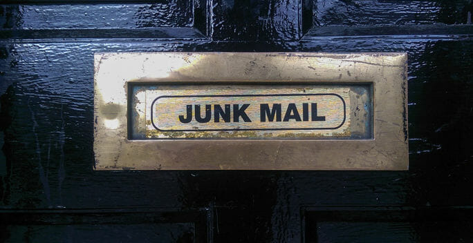 Gold door mail slot that says junk mail on black door.