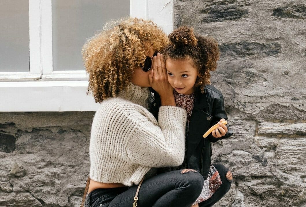 Modern mother squatting whispering into daughter’s ear