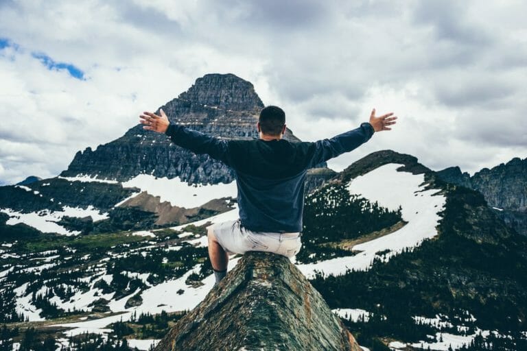 Man on top of mountain with arms out, embracing the view and freedom