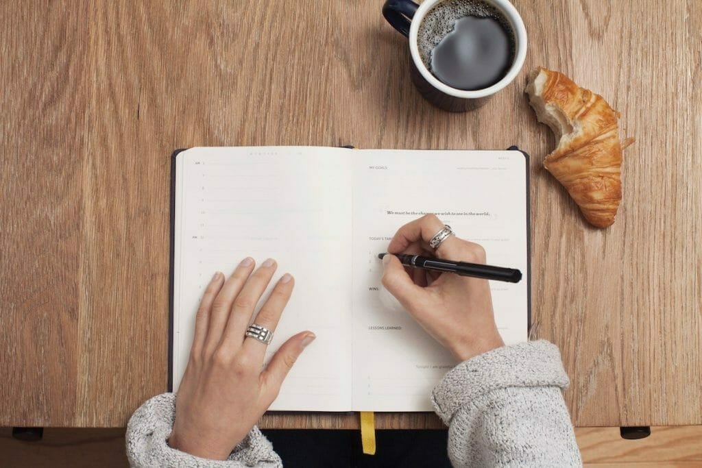 Writing in notebook with coffee and croissant