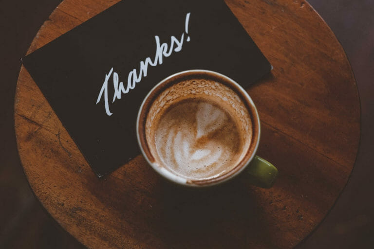 Thank you written on napkin under coffee on wooden table.