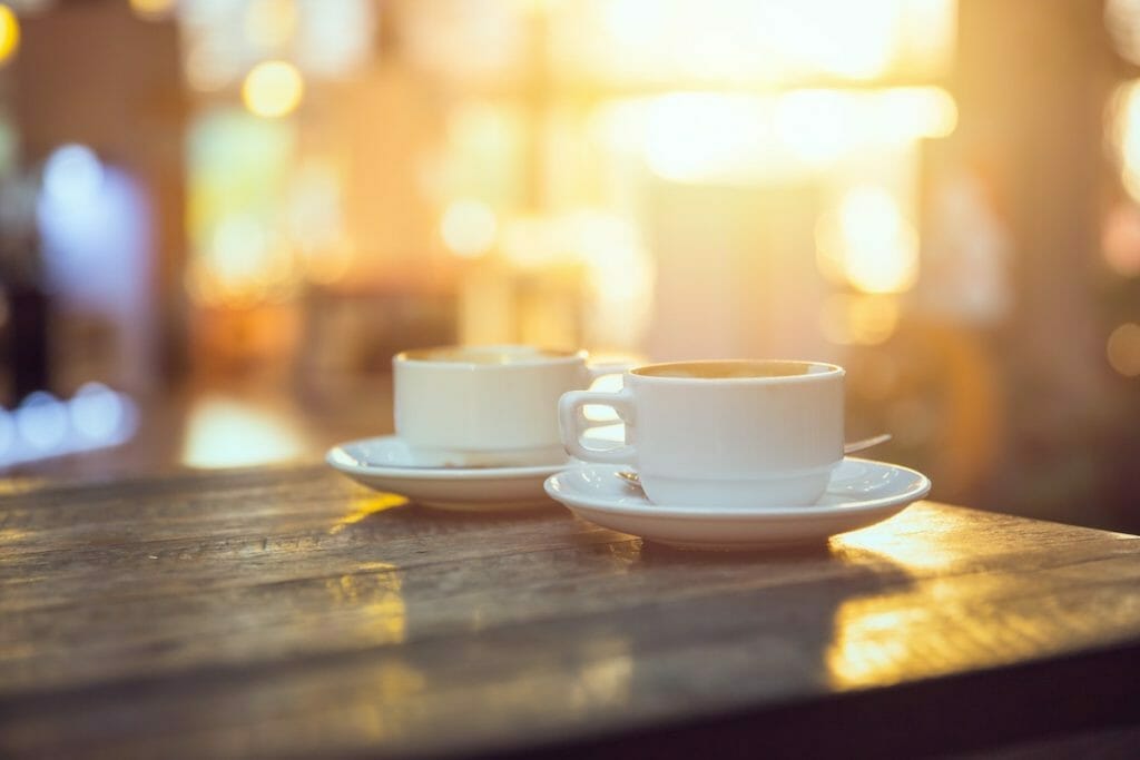Two cappuccinos basking in morning light on a wooden table at a coffee shop
