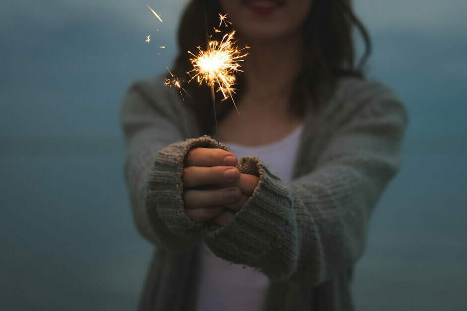 Woman in sweater holding sparkler at dusk